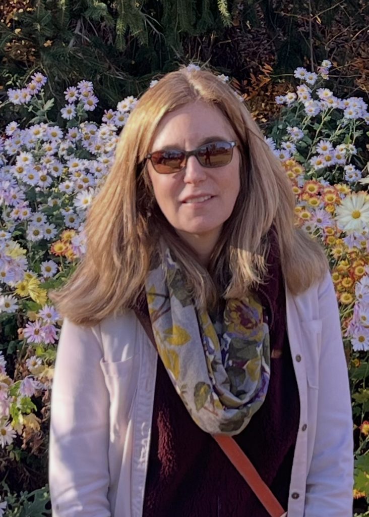 Woman in sunglasses smiling with background full of flowers.